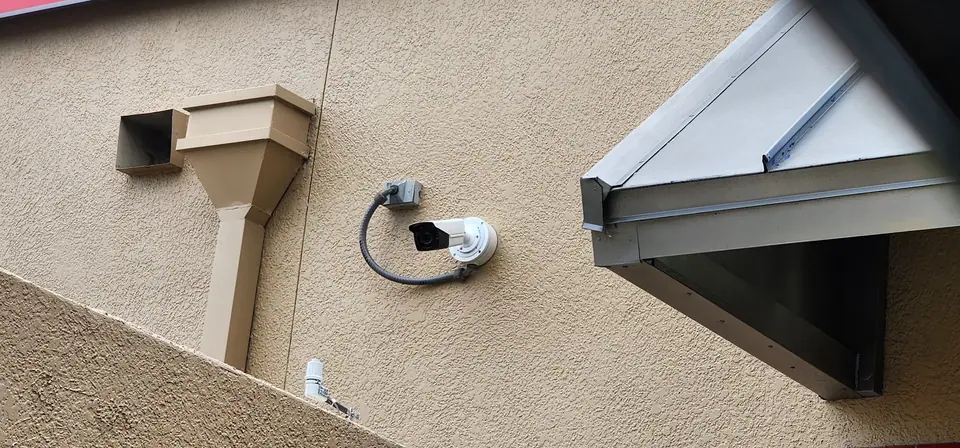 A bullet security camera beside a downspout on a tan stucco wall