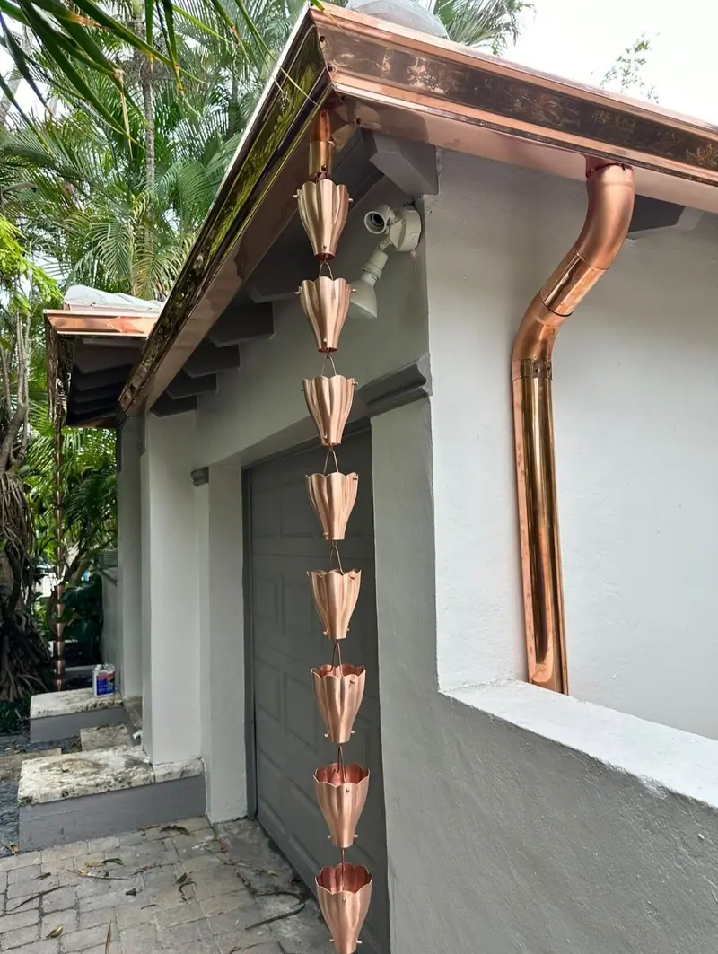 Copper gutter, downspout and rain chain on a white stucco home, with a security camera on the wall