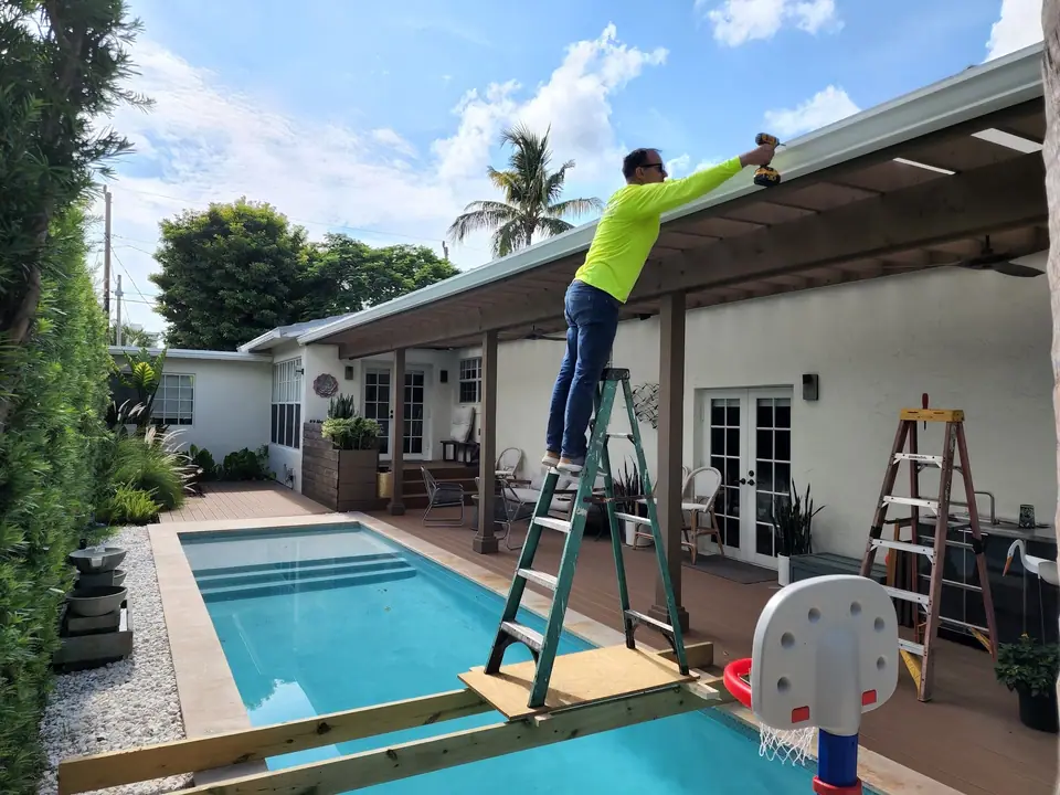 A crew member on a ladder working on a patio gutter beside a pool