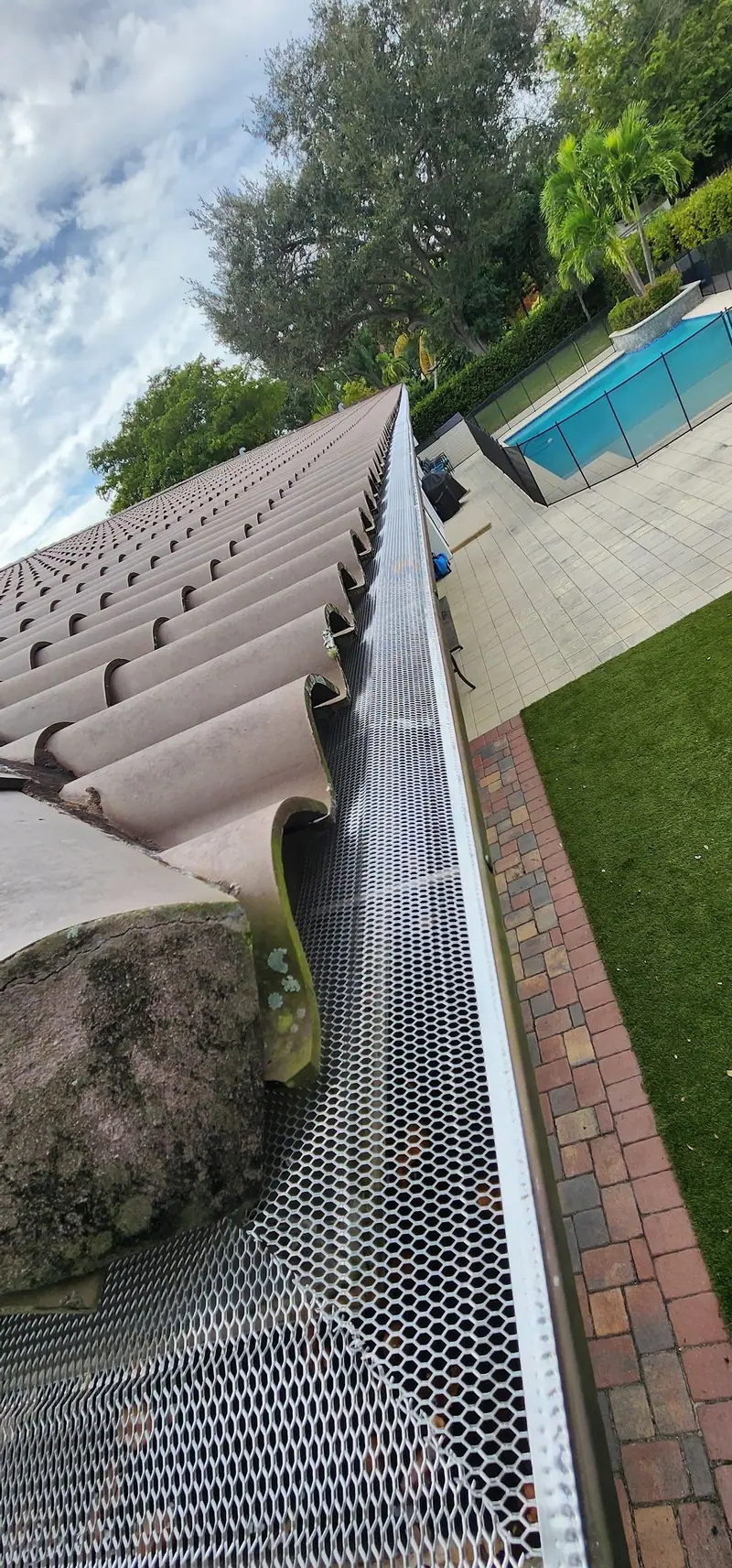 Mesh gutter guard installed along a tile roof beside a pool