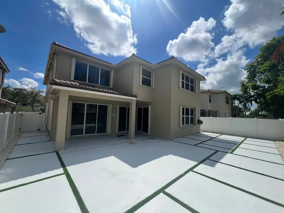New white gutters on a two-storey tan stucco home with a paver driveway
